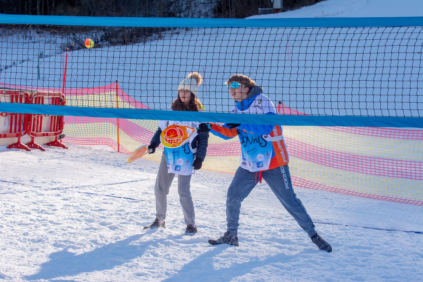 Due giocatori si affrontano a rete sul campo di Snow Tennis, pallina in volo